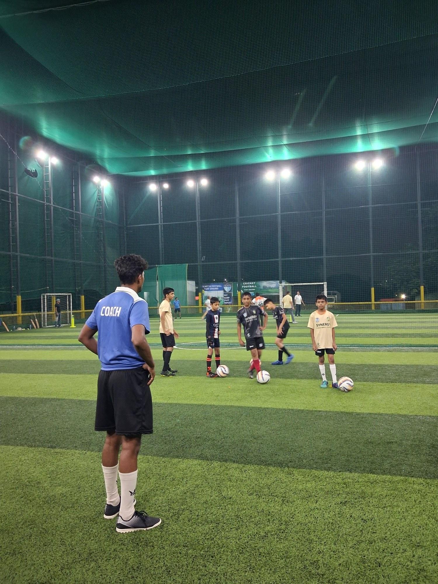Synergy FC children drilling under floodlights with a coach supervising